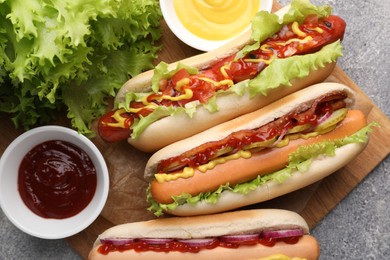 Photo of Delicious hot dogs with different toppings served on grey table, flat lay