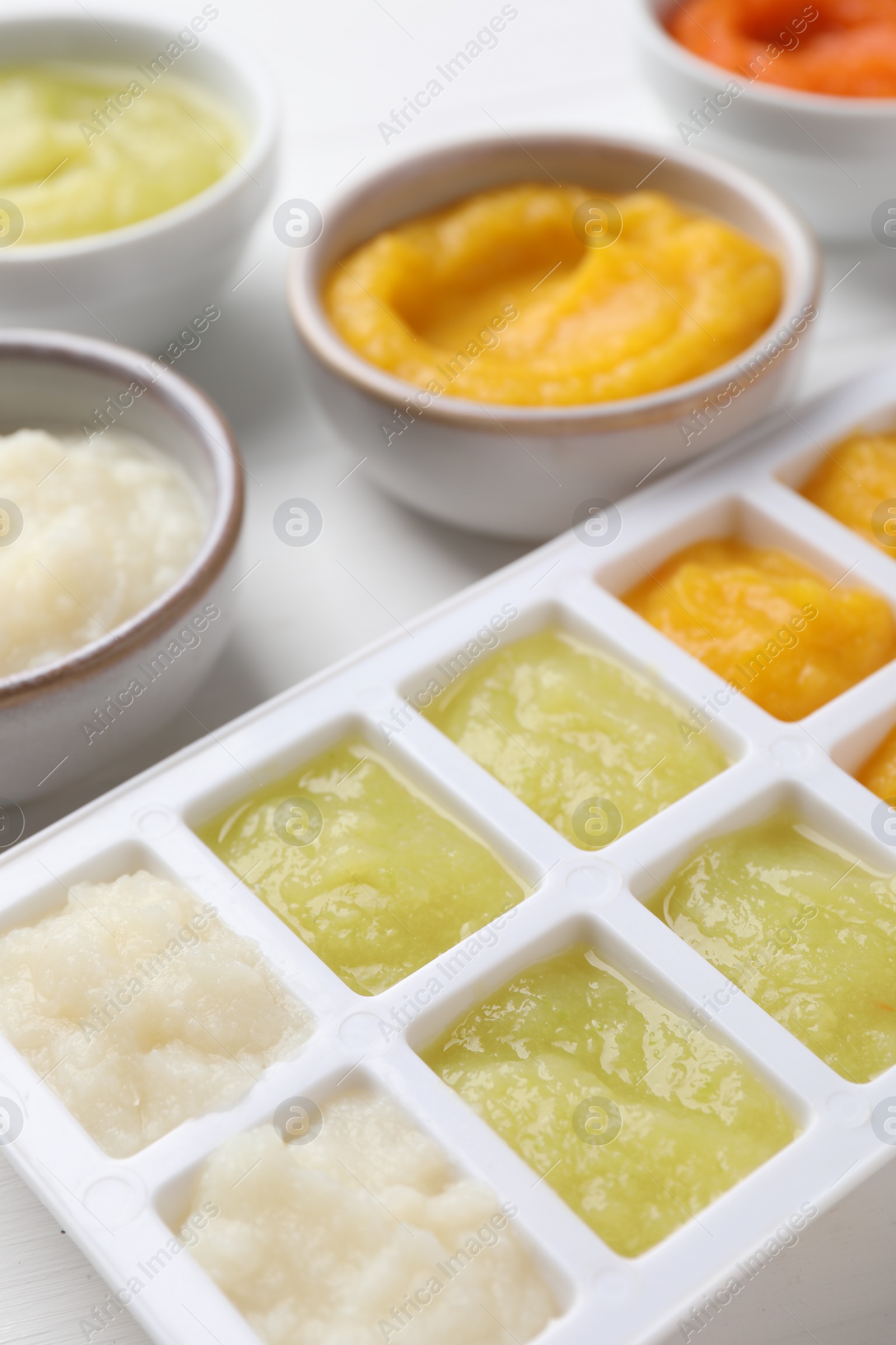 Photo of Different purees in ice cube tray and bowls on white table, closeup. Ready for freezing