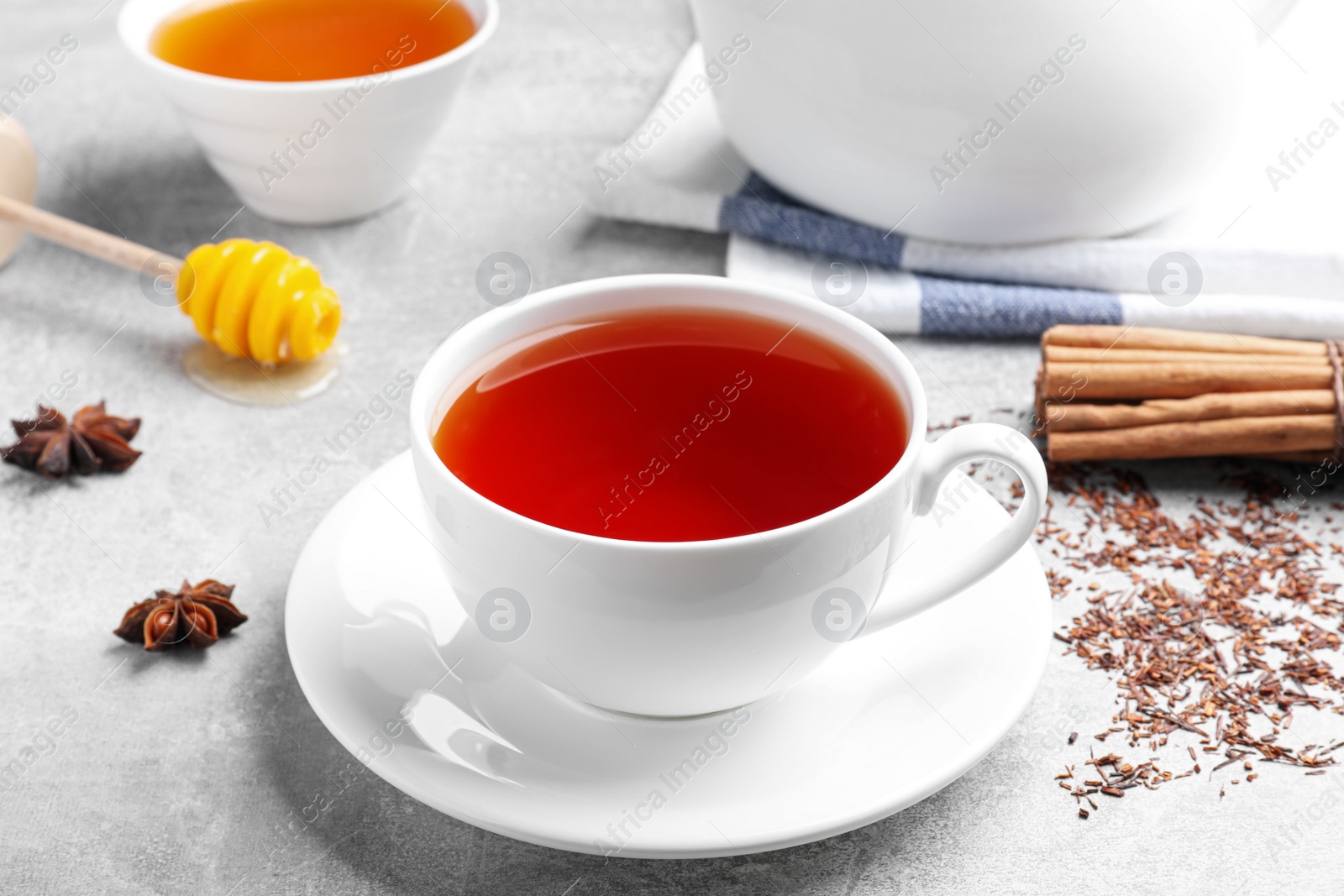 Photo of Freshly brewed rooibos tea, scattered dry leaves and spices on grey table