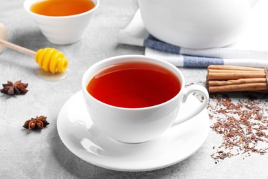 Freshly brewed rooibos tea, scattered dry leaves and spices on grey table