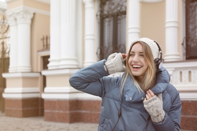 Photo of Young woman with headphones listening to music outdoors. Space for text