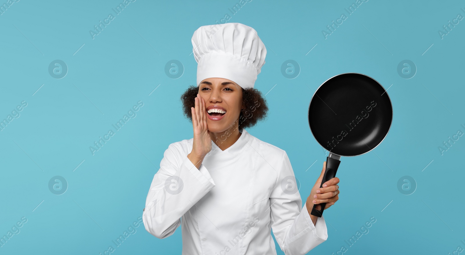 Photo of Happy female chef in uniform holding frying pan on light blue background