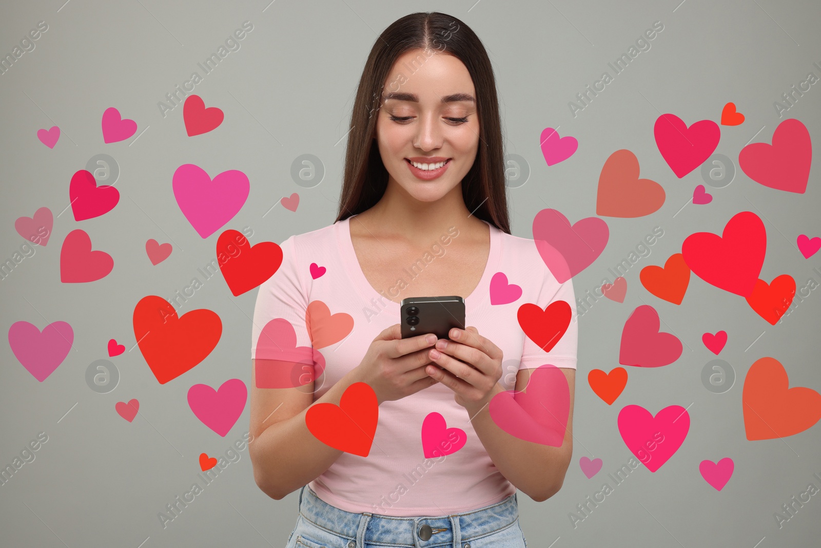 Image of Long distance love. Woman chatting with sweetheart via smartphone on grey background. Hearts flying out of device and swirling around her