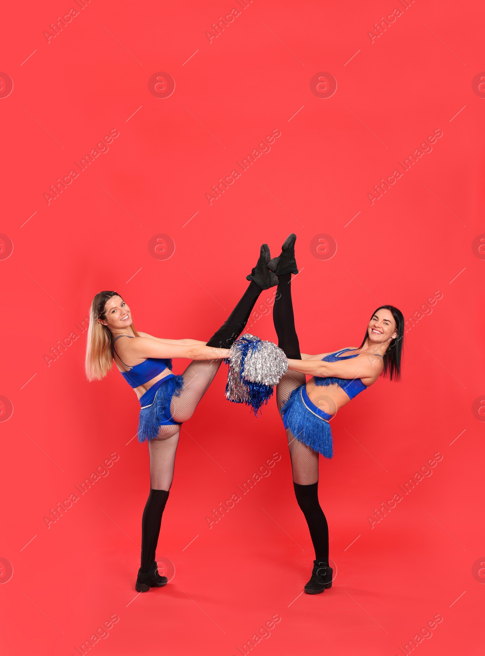 Photo of Beautiful young cheerleaders dancing on red background