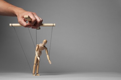 Photo of Man pulling strings of puppet on gray background, closeup. Space for text
