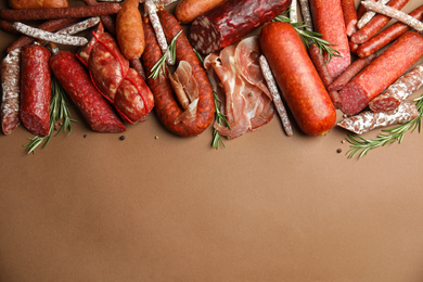 Photo of Different types of sausages with rosemary on brown background, flat lay. Space for text