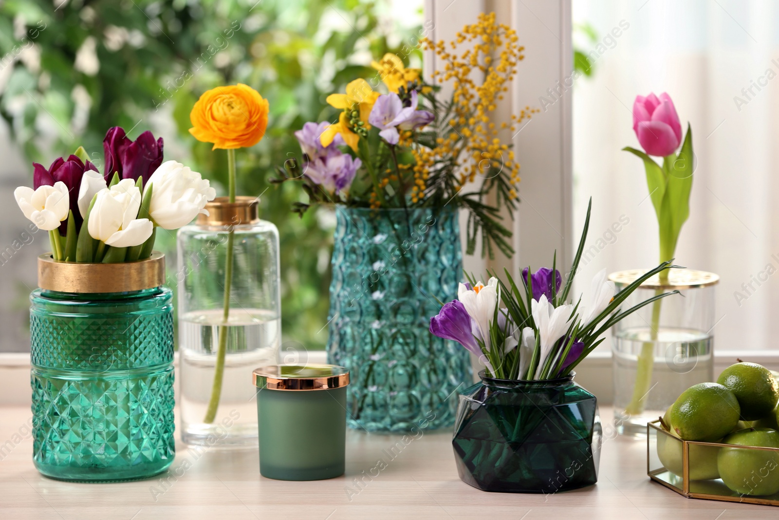 Photo of Different beautiful spring flowers and candle on window sill