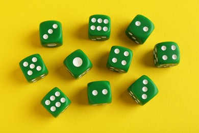 Photo of Many green game dices on yellow background, flat lay