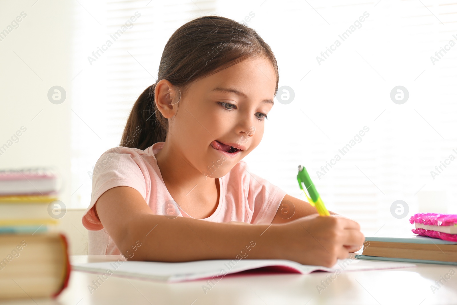 Photo of Little girl doing homework at table indoors