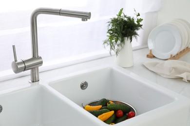 Photo of Modern sink with water tap and fresh vegetables near window in kitchen