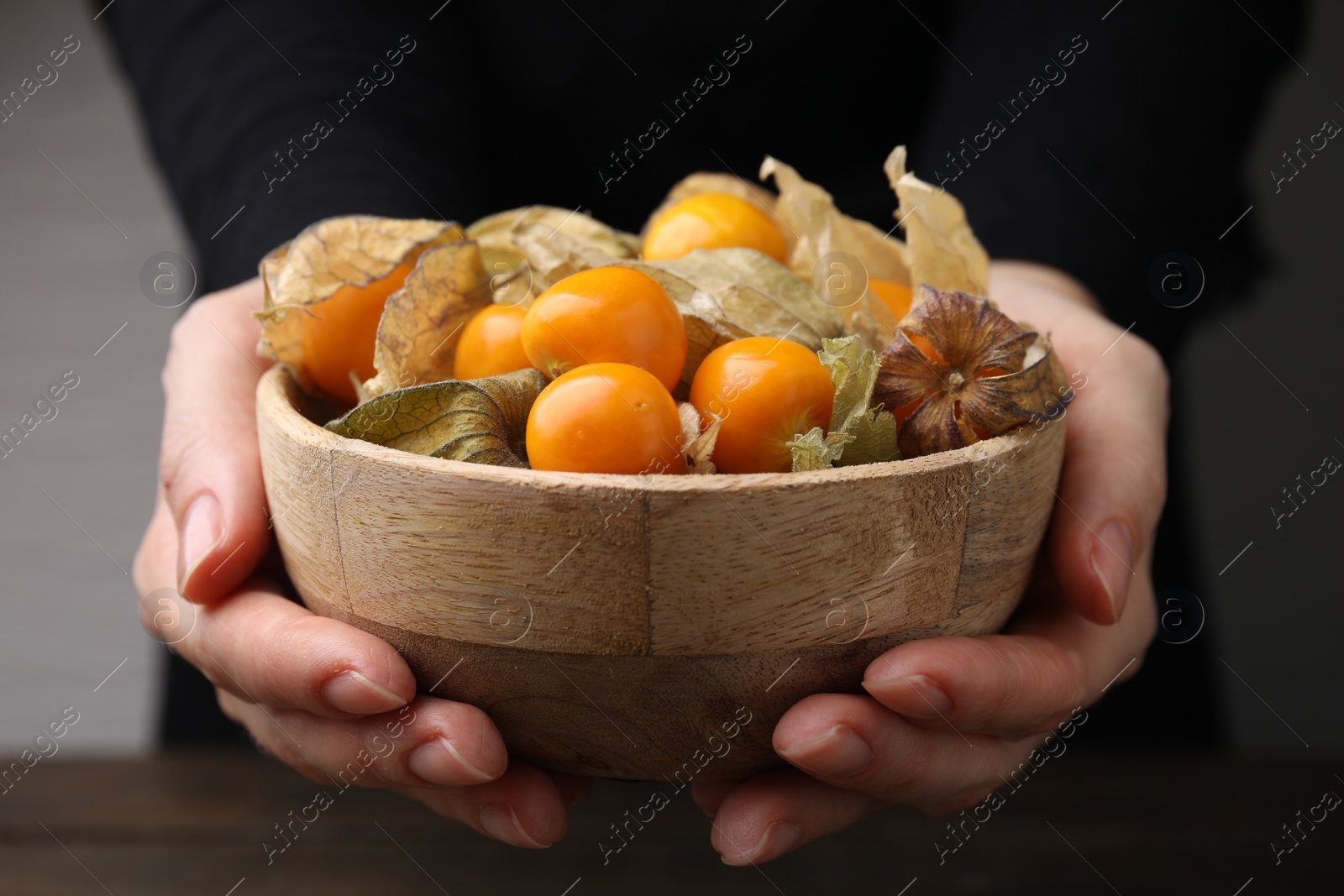 Photo of Woman holding bowl with ripe physalis fruits and calyxes, closeup