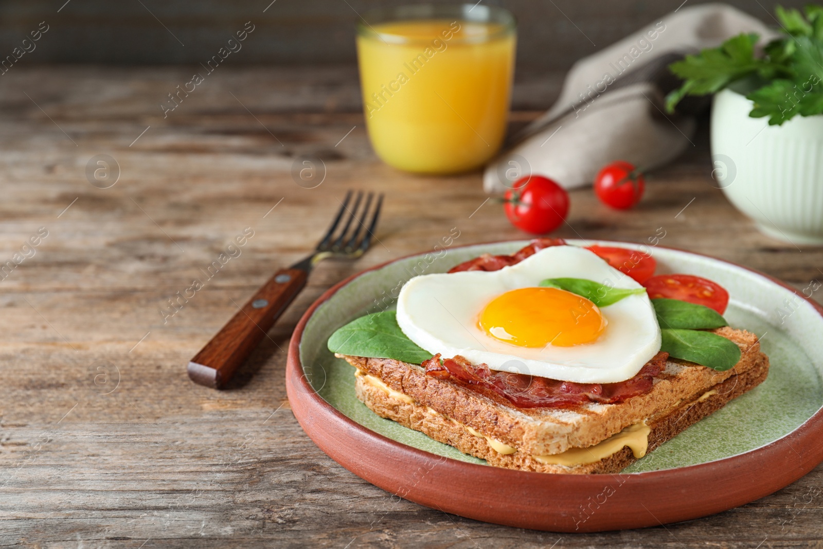 Photo of Plate of tasty sandwich with heart shaped fried egg and  bacon on wooden table