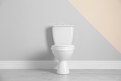 Photo of New toilet bowl near color wall indoors