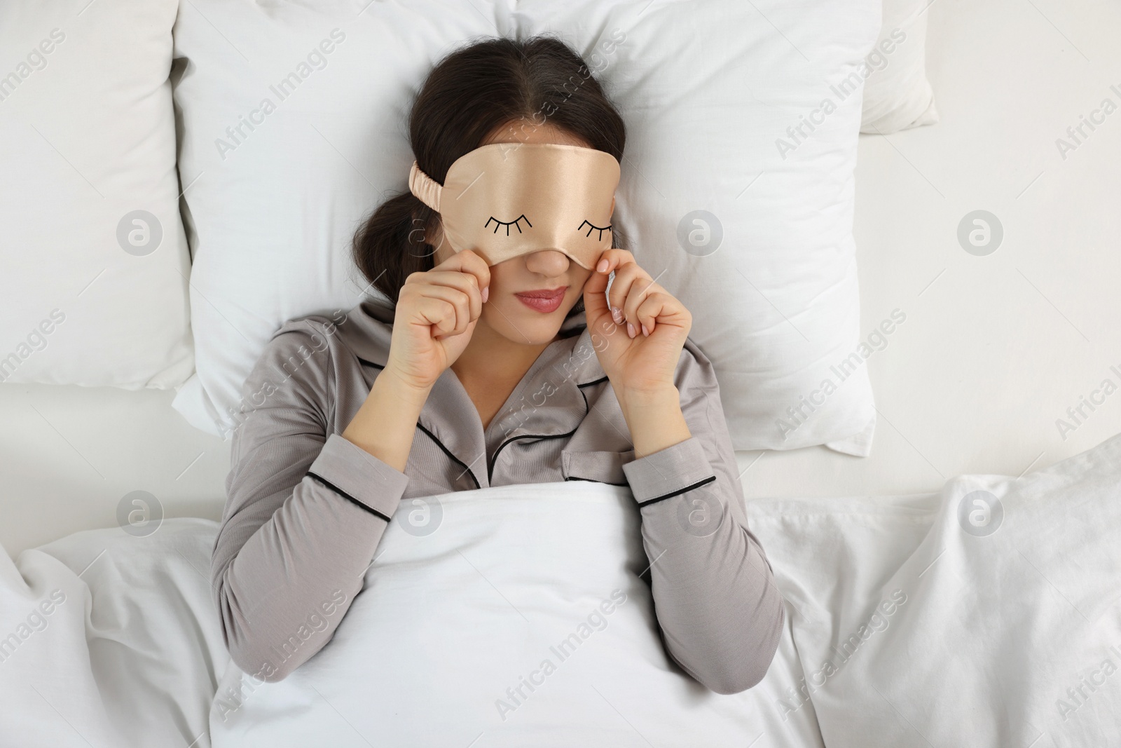 Image of Young woman with sleeping mask in bed, top view. Problem of sleep deprivation