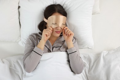 Image of Young woman with sleeping mask in bed, top view. Problem of sleep deprivation