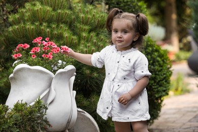 Photo of Cute little girl near pink flowers in park