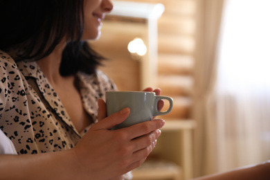 Photo of Young woman in pajamas with drink at home, closeup. Lazy morning