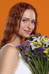 Photo of Beautiful young hippie woman with bouquet of colorful flowers on orange background, closeup