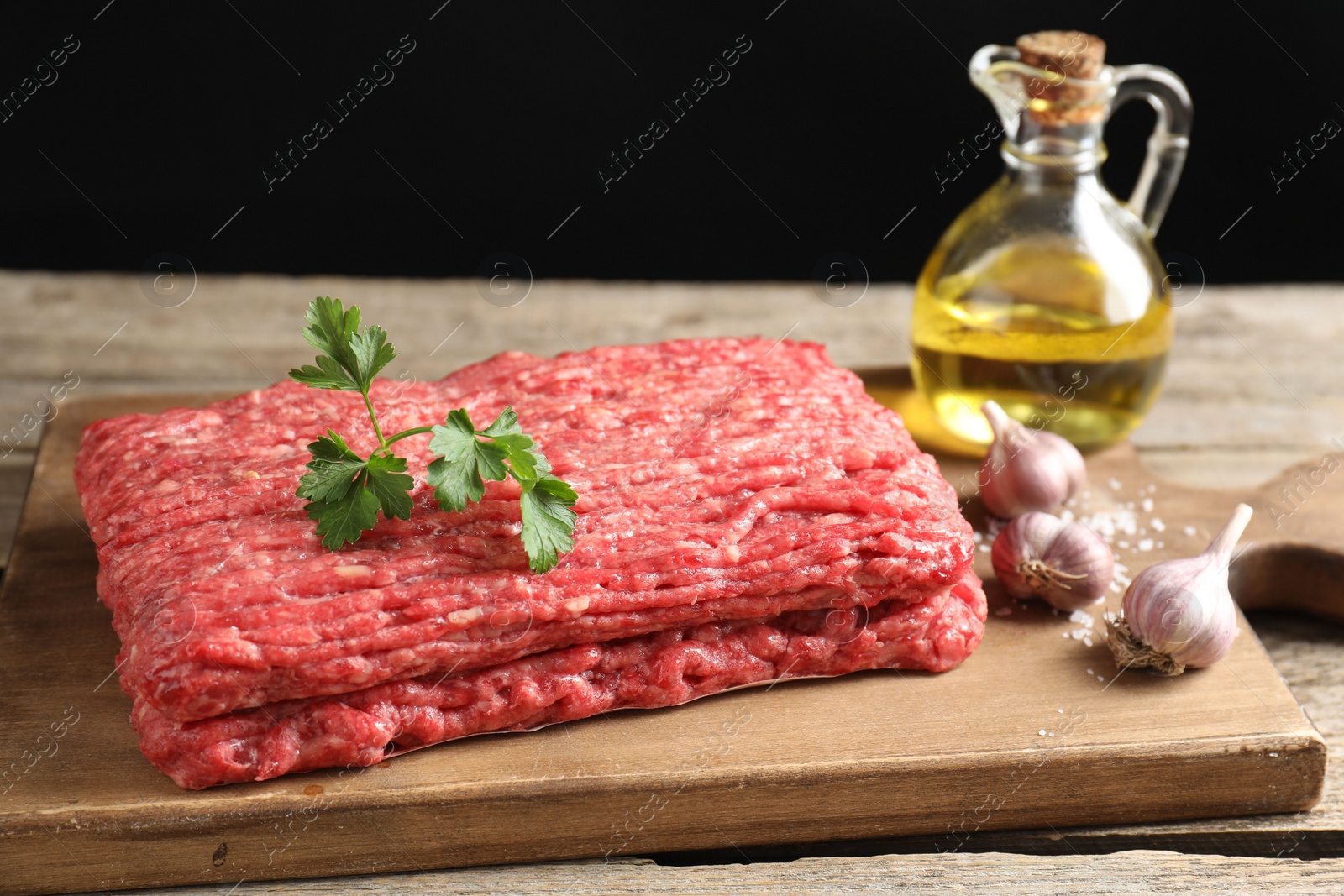 Photo of Raw ground meat, garlic, oil and parsley on wooden table