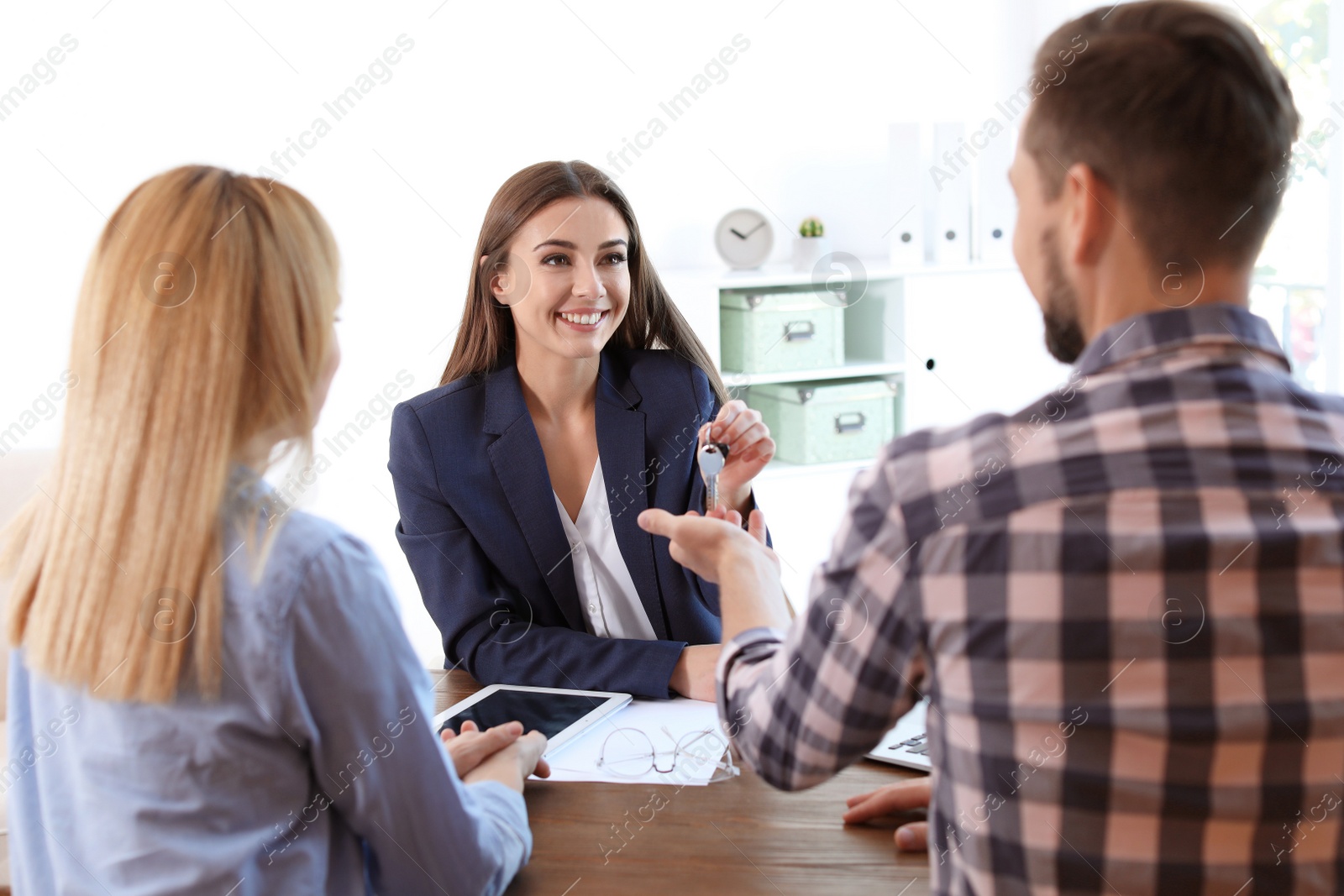 Photo of Female real estate agent giving house key to couple at table in office