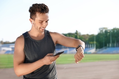 Young sportsman with wireless earphones, mobile phone and smart watch at stadium