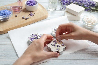 Young woman making handmade soap bar with lavender flowers on white wooden background, closeup