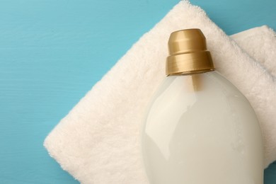 Photo of Bottle of fabric softener and towel on light blue wooden table, top view. Space for text