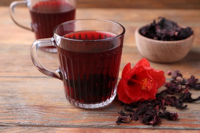 Photo of Delicious hibiscus tea and dry flowers on wooden table