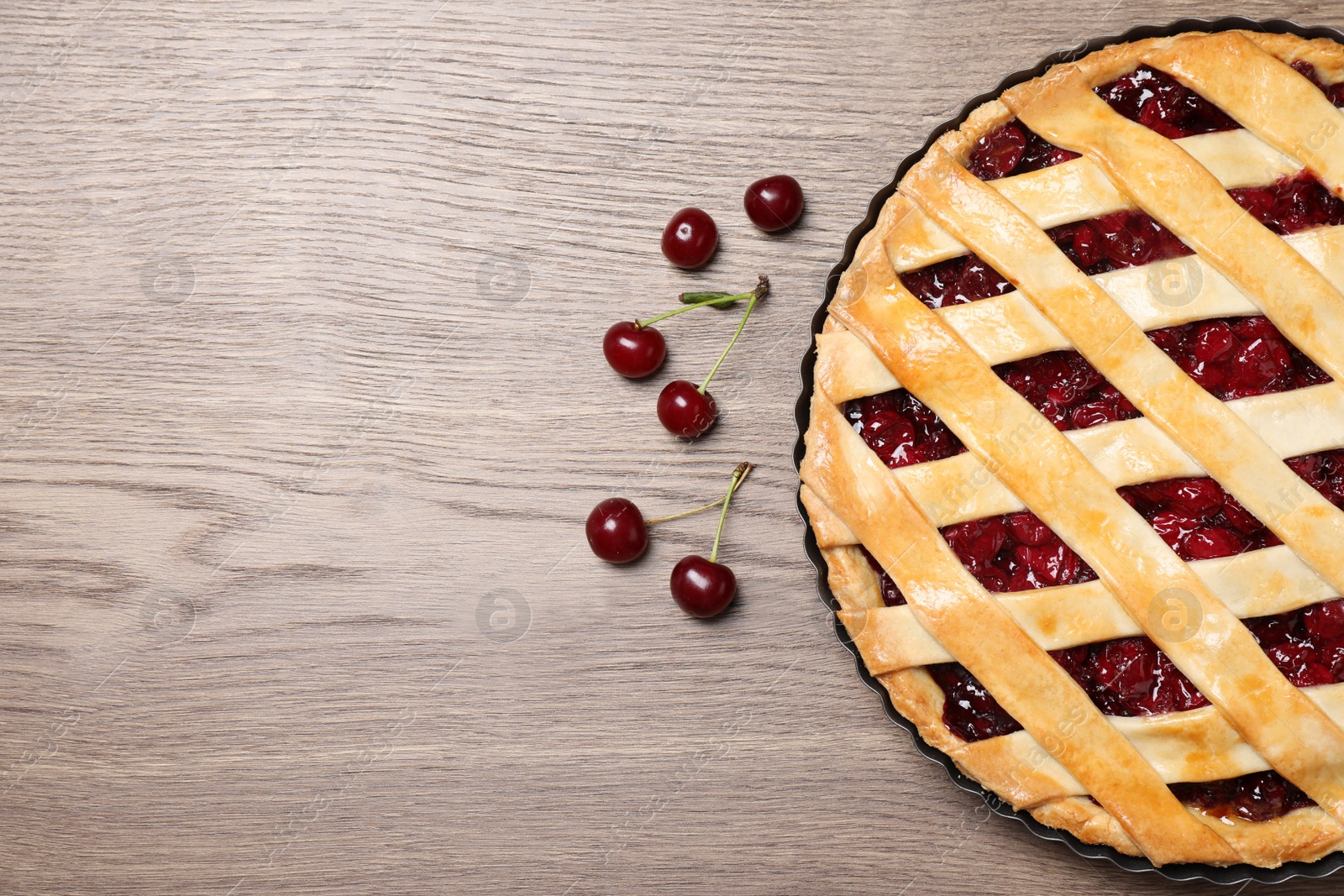 Photo of Delicious fresh pie and cherries on wooden table, flat lay. Space for text