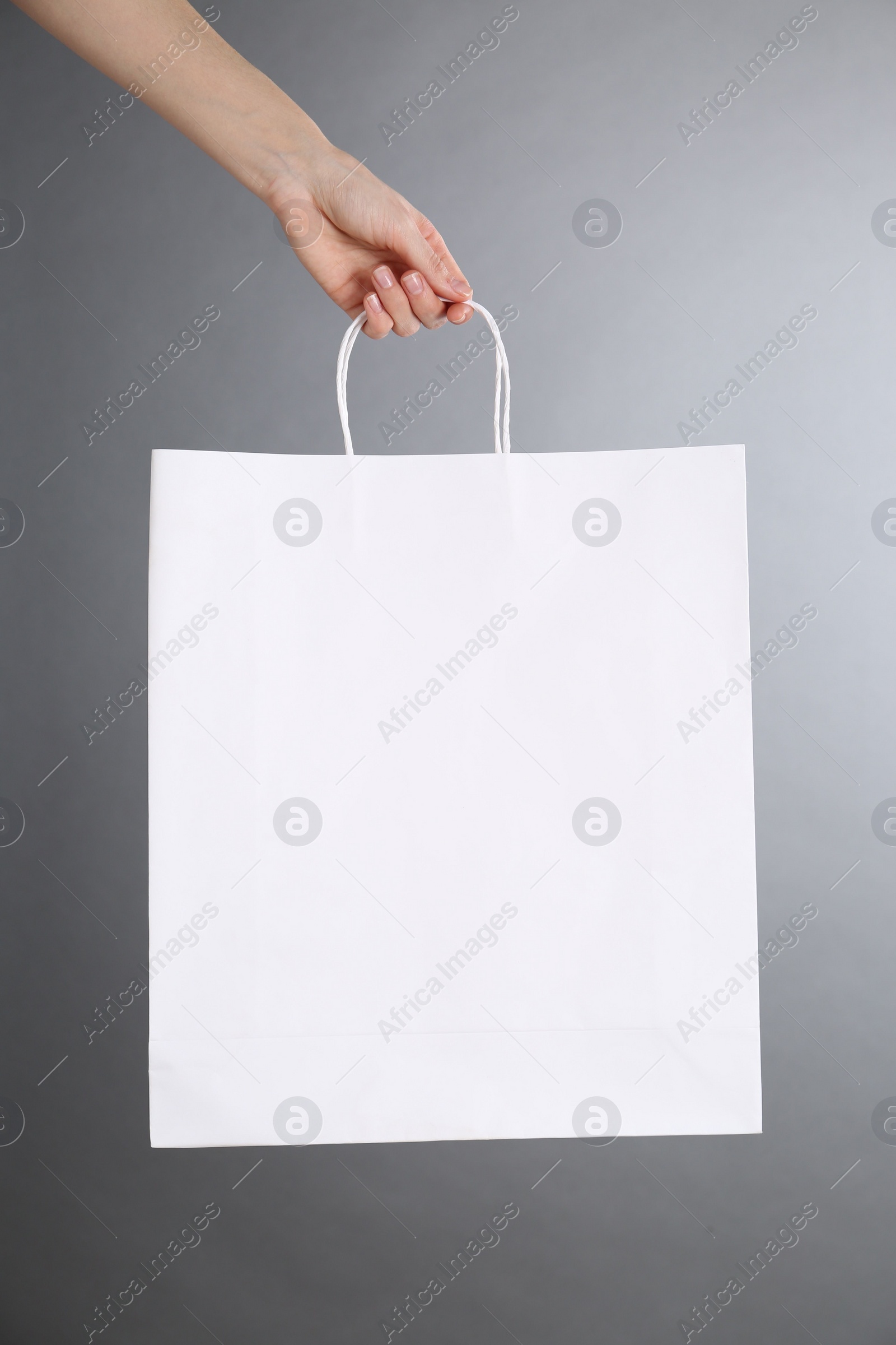 Photo of Woman holding white paper bag on grey background, closeup. Mockup for design