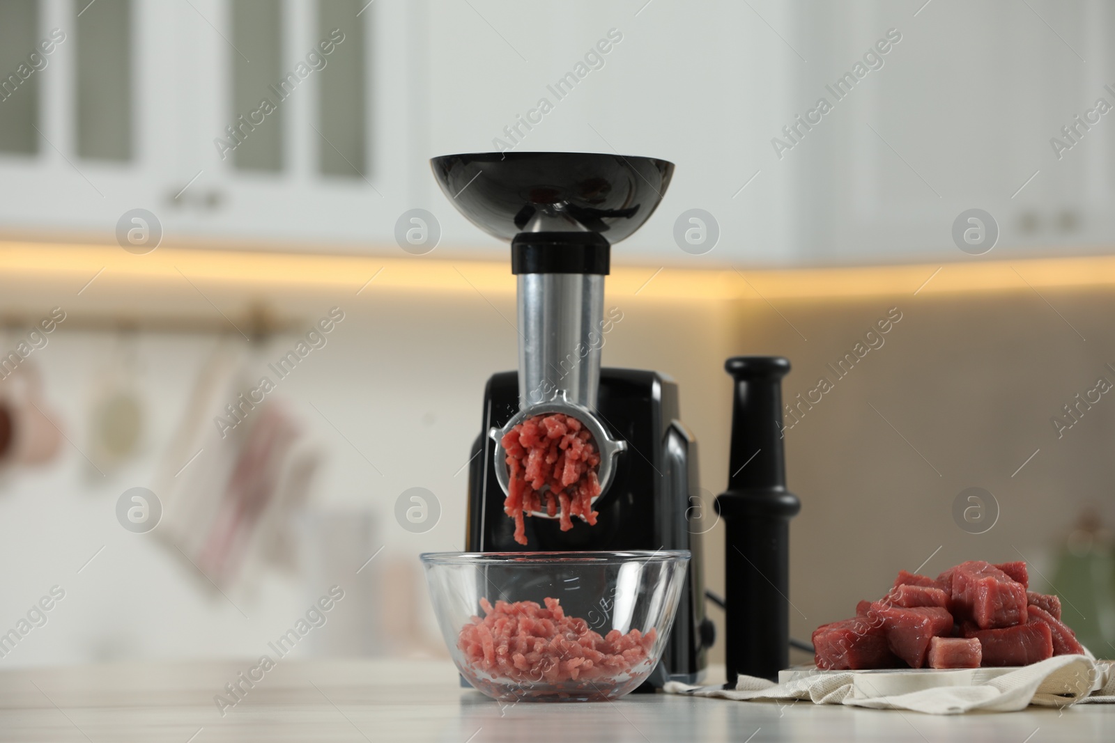 Photo of Electric meat grinder with beef mince on white table in kitchen