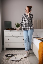 Photo of Young woman listening to music with turntable in bedroom
