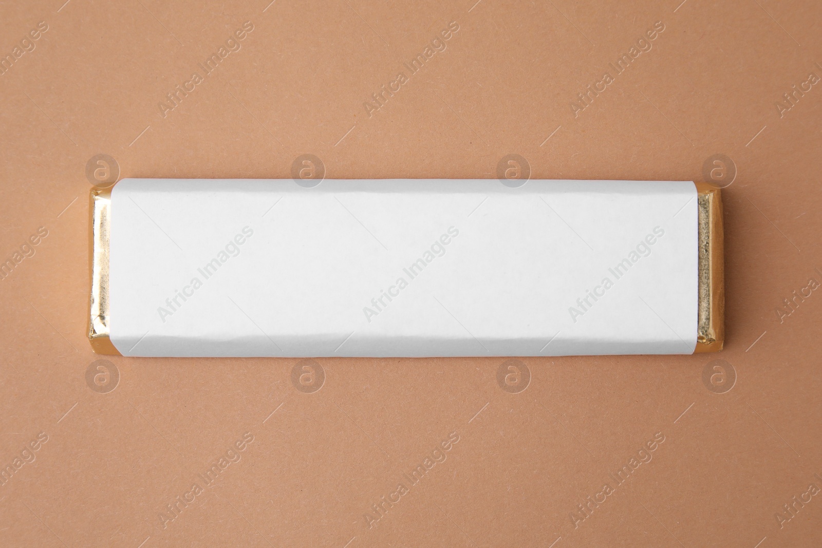 Photo of Tasty chocolate bar in package on light brown background, top view