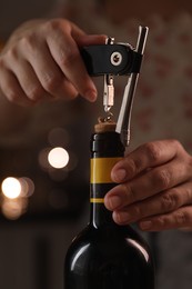 Photo of Woman opening wine bottle with corkscrew on blurred background, closeup