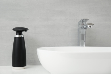 Modern automatic soap dispenser near sink in bathroom, closeup