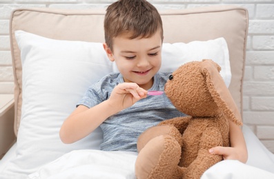 Photo of Cute child playing doctor with stuffed toy in bed at hospital