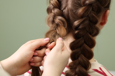 Photo of Professional stylist braiding woman's hair on olive background, closeup