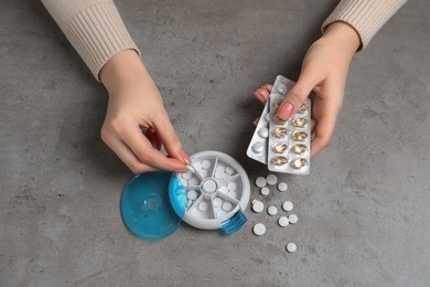 Woman putting pill into plastic box at grey table, top view