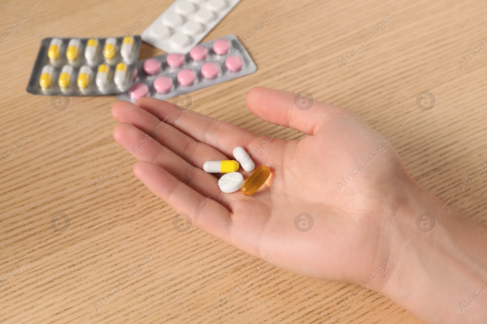 Photo of Man holding pills at wooden table, closeup