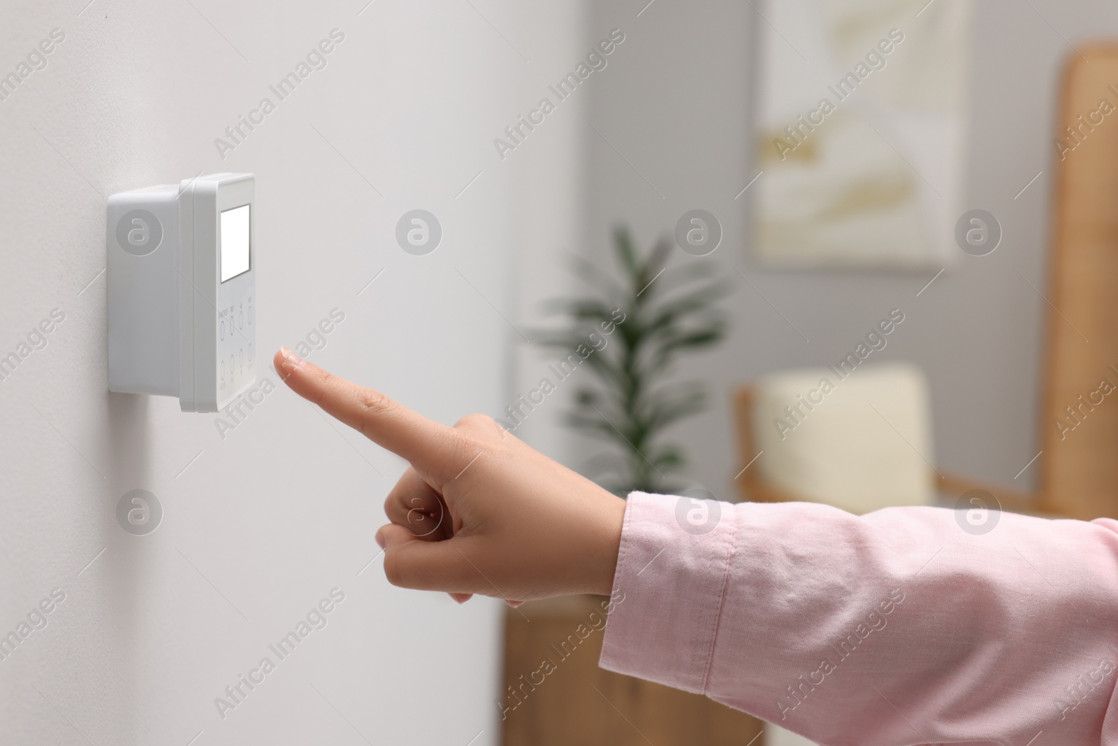 Photo of Woman adjusting thermostat on white wall indoors, closeup. Smart home system