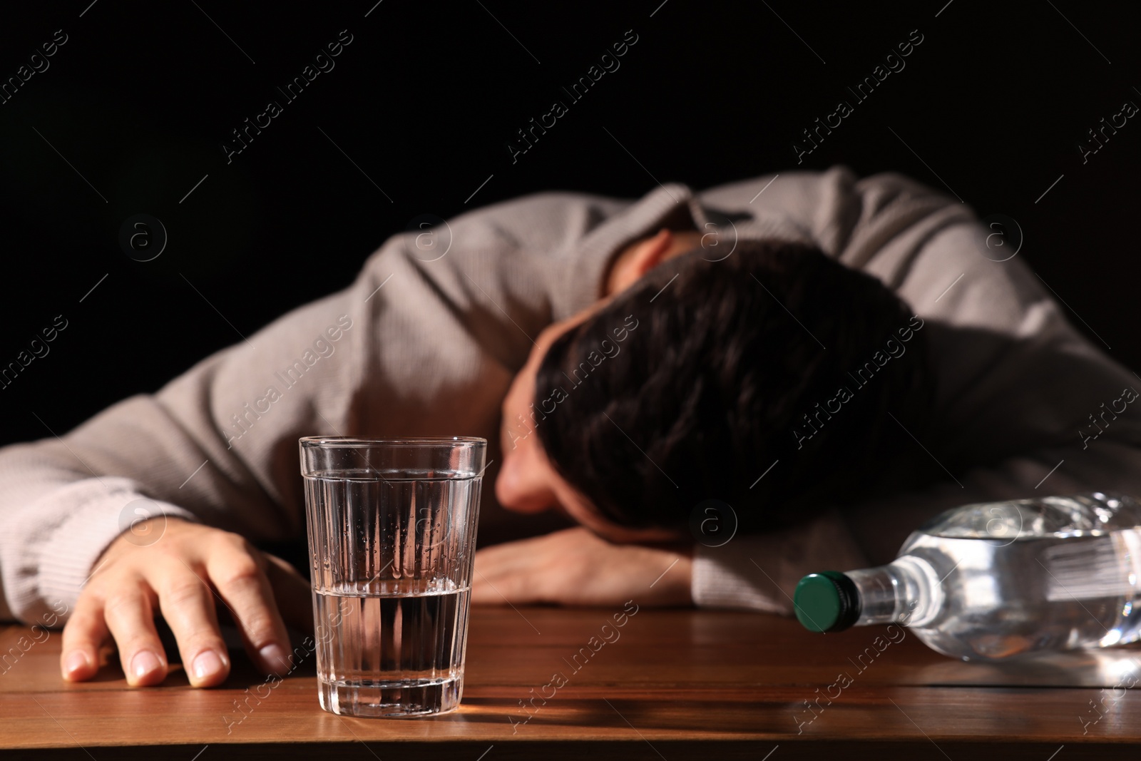 Photo of Addicted man with alcoholic drink at wooden table against black background, focus on glass