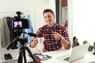 Photo of Fashion blogger with cup of coffee recording video on camera at home