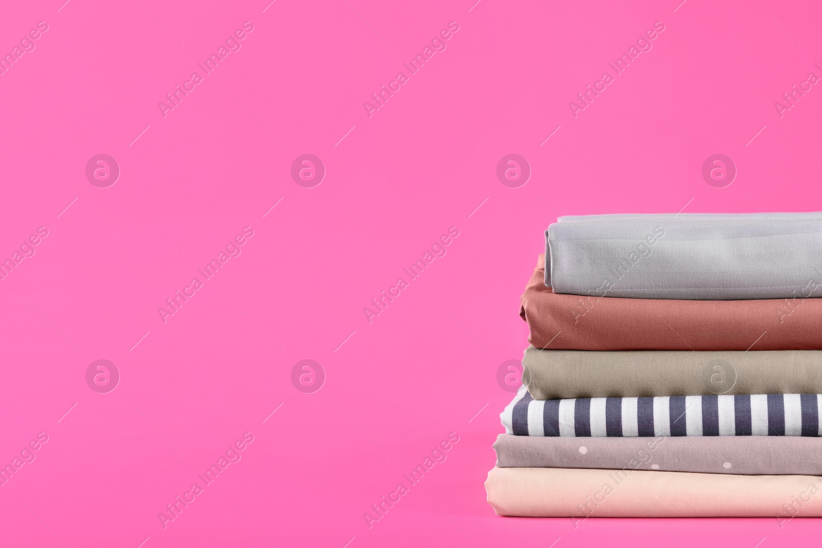 Photo of Stack of clean bed sheets on pink background. Space for text