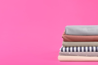 Stack of clean bed sheets on pink background. Space for text