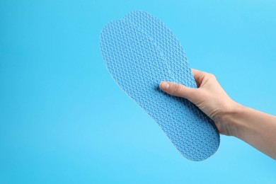 Photo of Woman holding pair of insoles on light blue background, closeup. Space for text