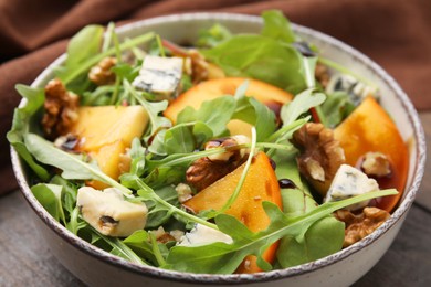 Photo of Tasty salad with persimmon, blue cheese and walnuts served on wooden table, closeup