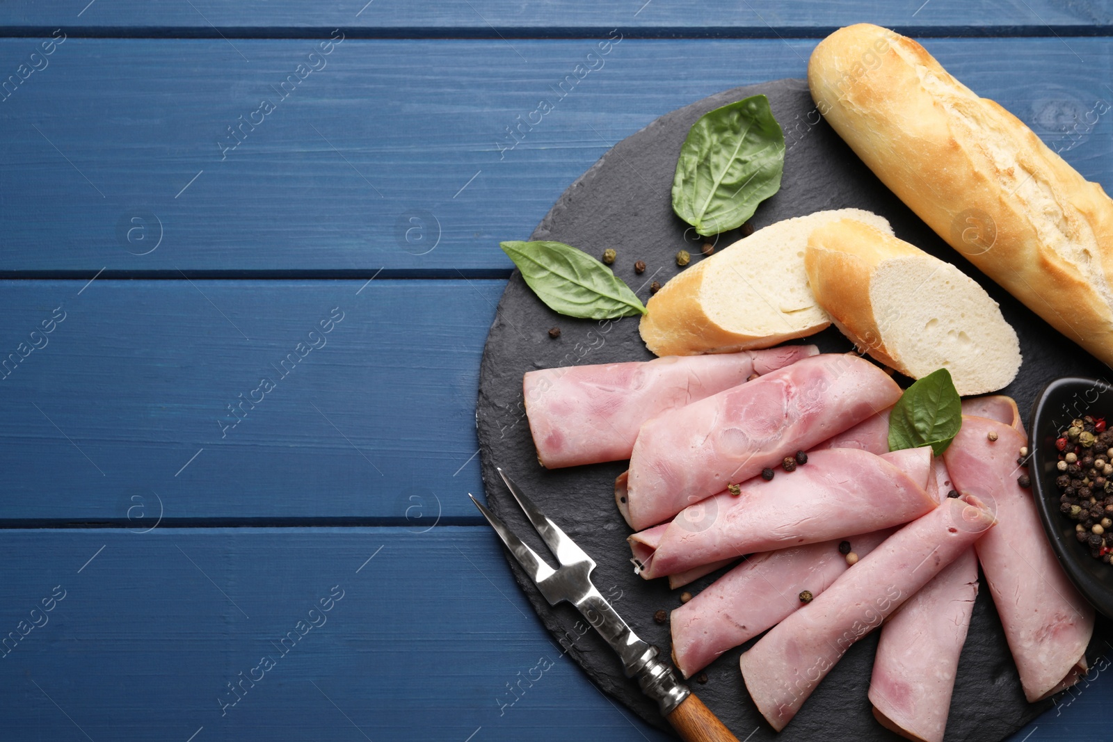Photo of Rolled slices of delicious ham and baguette served on blue wooden table, flat lay. Space for text