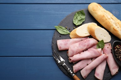 Photo of Rolled slices of delicious ham and baguette served on blue wooden table, flat lay. Space for text