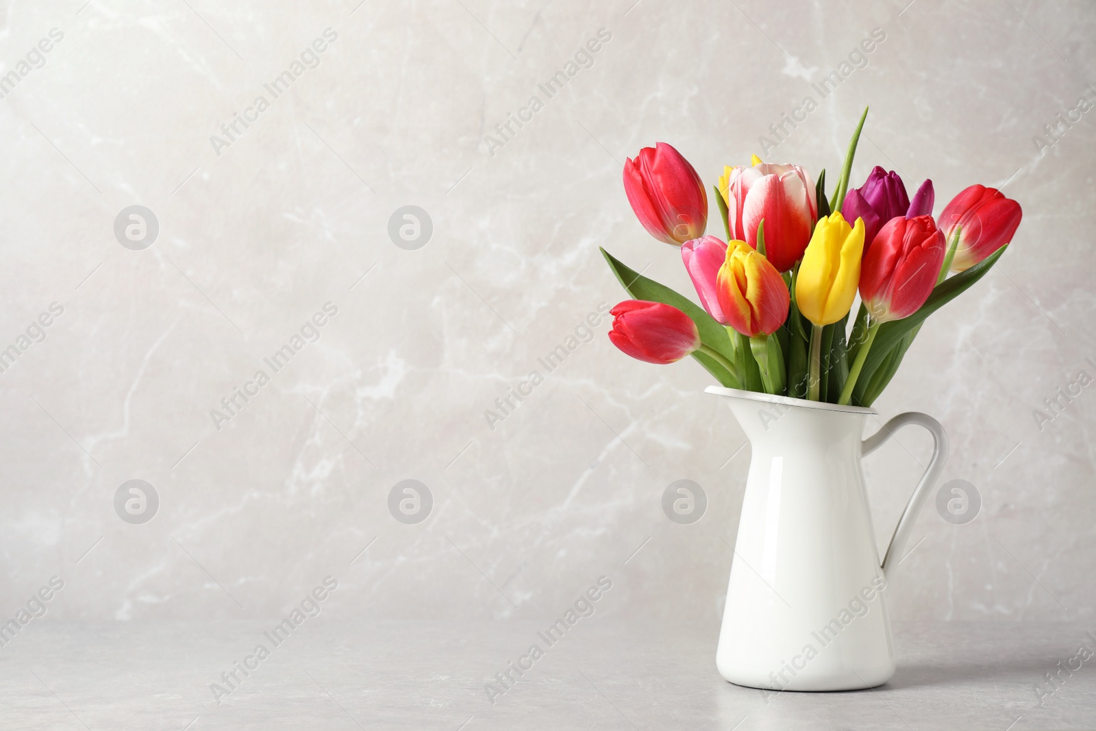 Photo of Beautiful spring tulips in vase on table against light marble background. Space for text