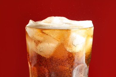 Glass of refreshing soda drink with ice cubes on red background, closeup